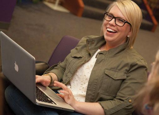 woman laughs while sitting in chair holding laptop
