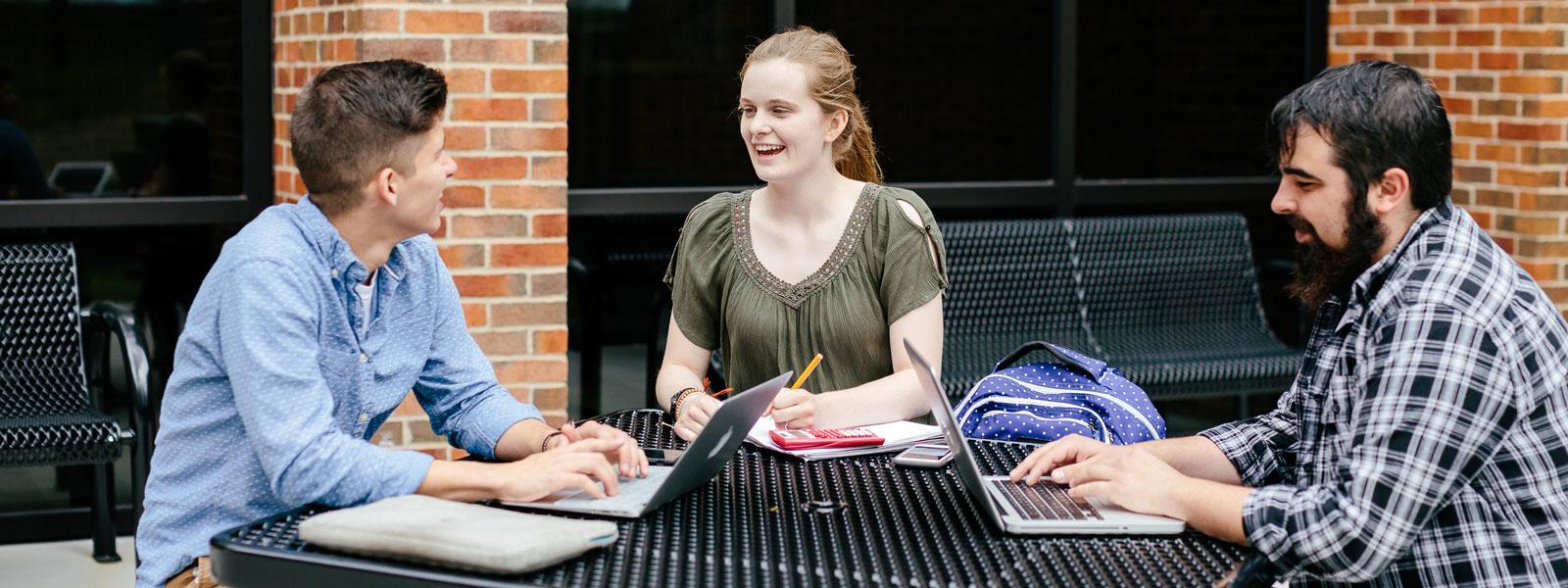 three students working on homework at outside picnic table