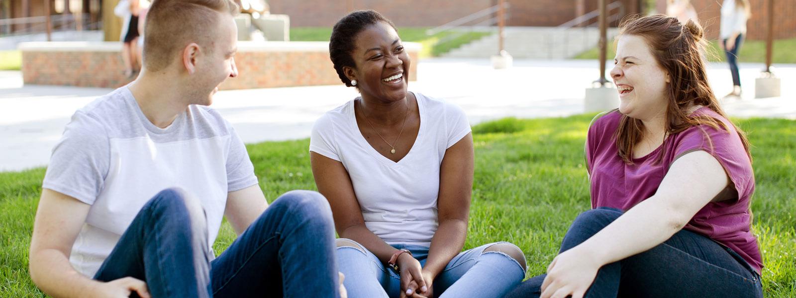 两个女同学和一个男同学坐在论坛的草地上笑