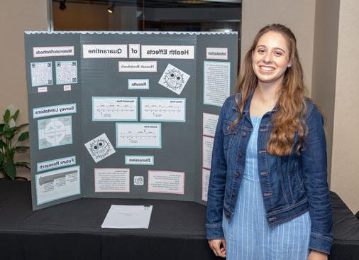 female student smiles next to research display board