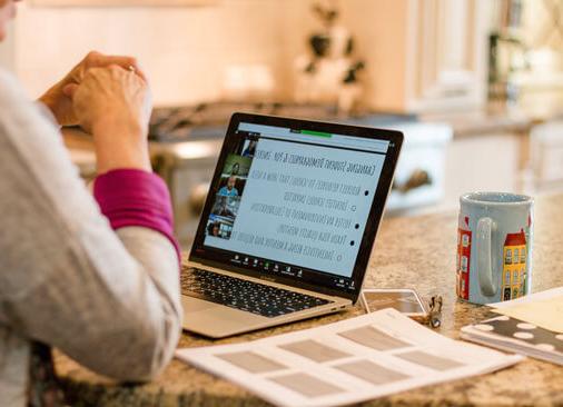 view from behind as teacher sits with laptop at kitchen table