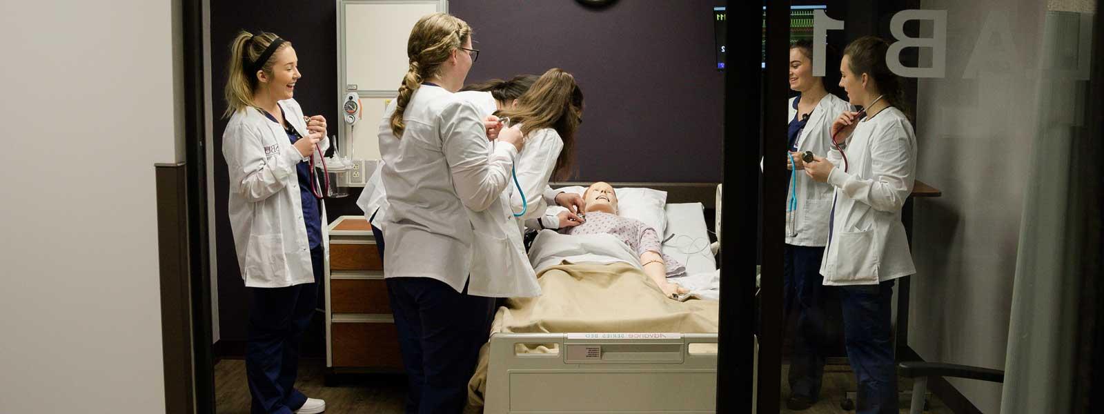 group of nursing students in simulation lab practicing listening to mannequin's heartbeat