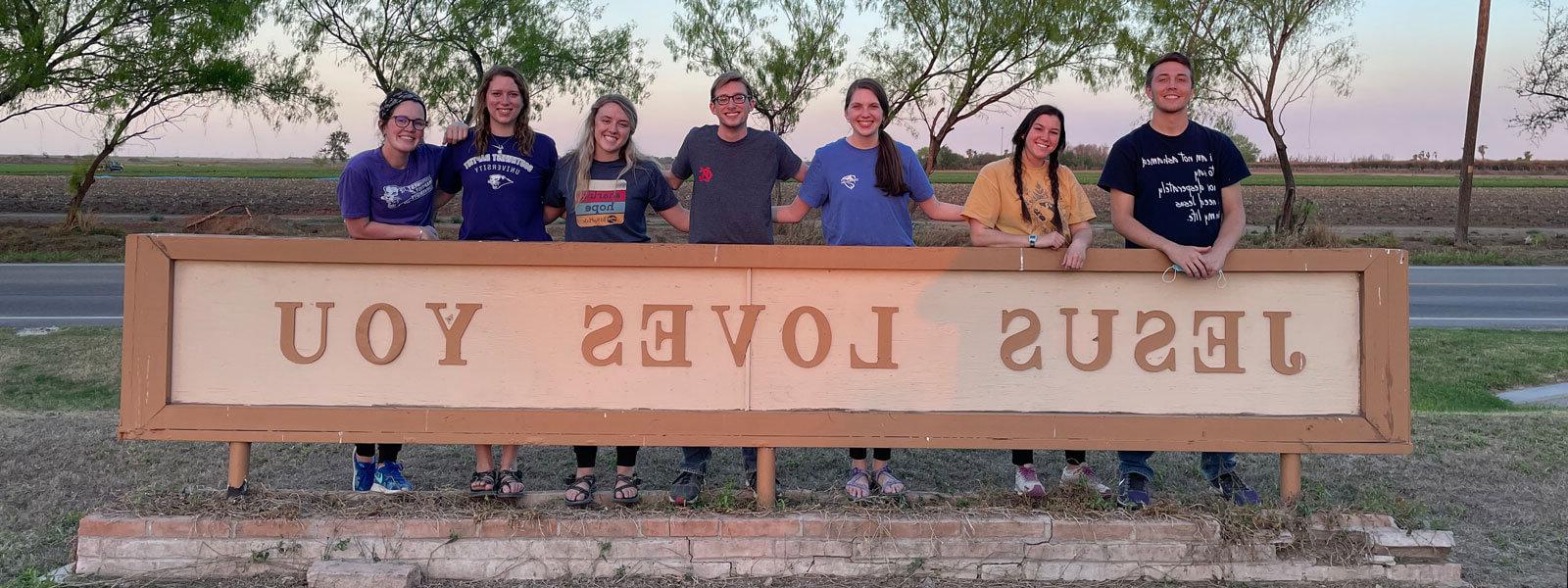 group of college students standing behind sign that says Jesus Loves you