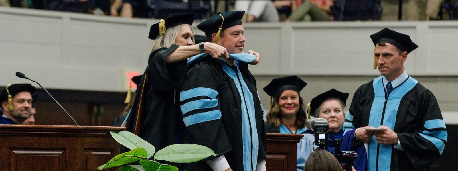 doctor of education graduate shakes president's hand as he receives diploma on graduation stage