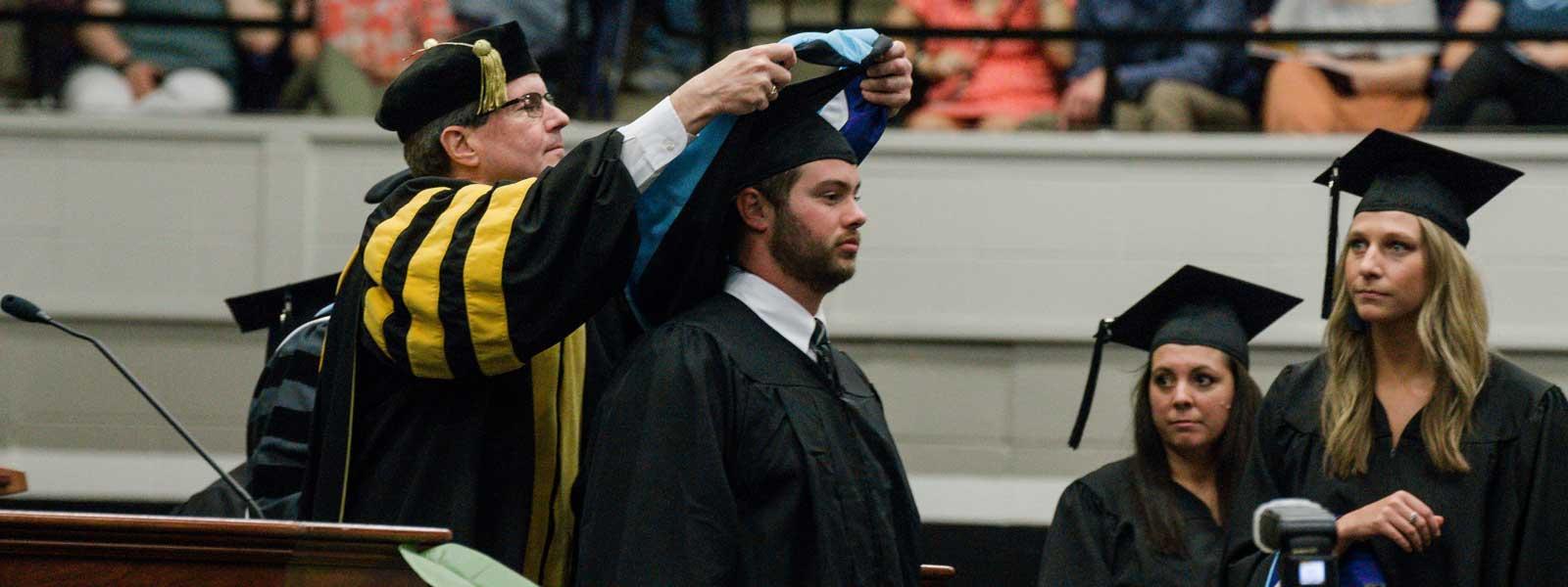 学院院长把兜帽套在毕业生的脖子上，而其他毕业生则在一旁观望，等待轮到他们
