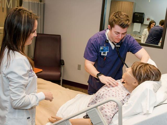 nursing student practices with mannequin with instructor looking on
